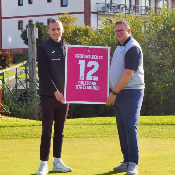 Zwei Männer auf dem Golfplatz, welche ein Trikot im Bilderrahmen tragen