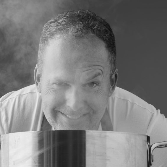 Mann schaut über einen Topf aus dem Dampf aufsteigt