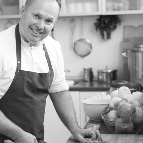 Mann mit Schürze steht an Arbeitsfläche in der Küche mit Arbeitsutensilien und Obst