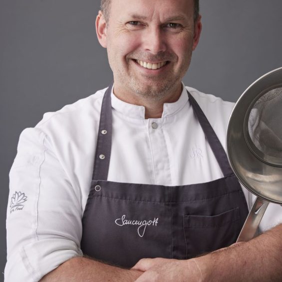 Koch mit Schürze und Pfanne lächelt